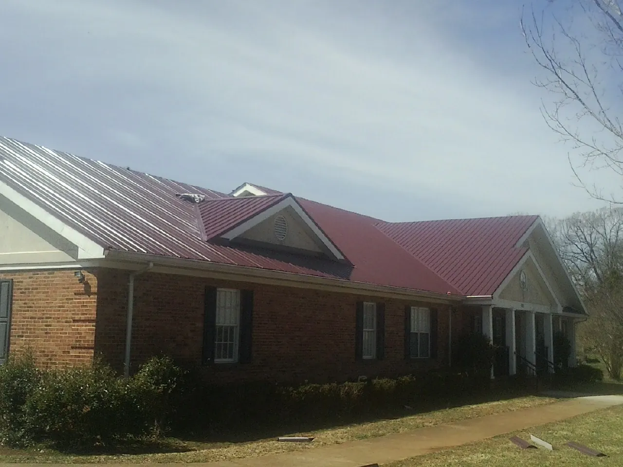 Red metal roof with gabled entries on a long brick building, from a Hail Damage Roof Repair job in Fairlee