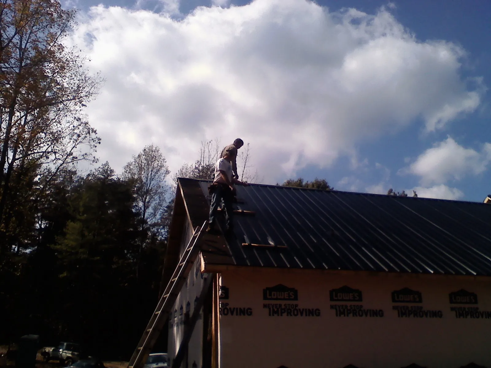 Roofer fastening dark metal panels high against a cloudy sky, from a Roof Inspection job in Fairlee